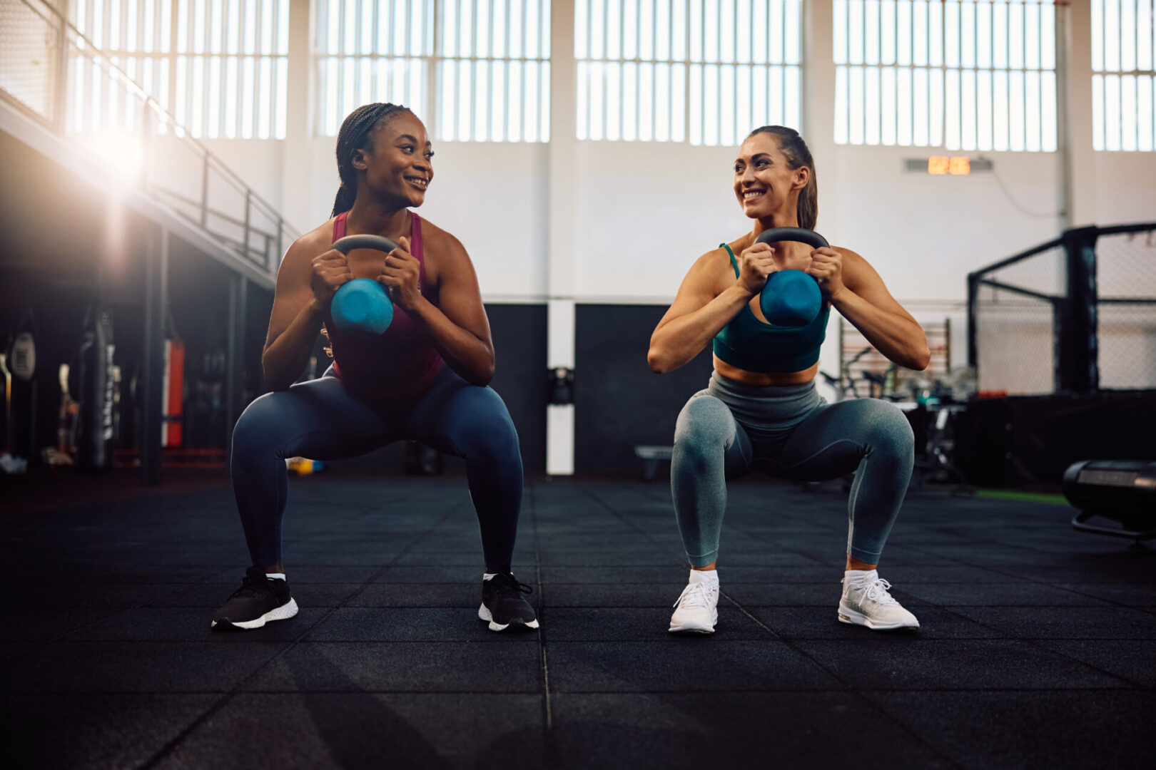 Here's an alt tag for the image: Two women kettlebell squats at gym.