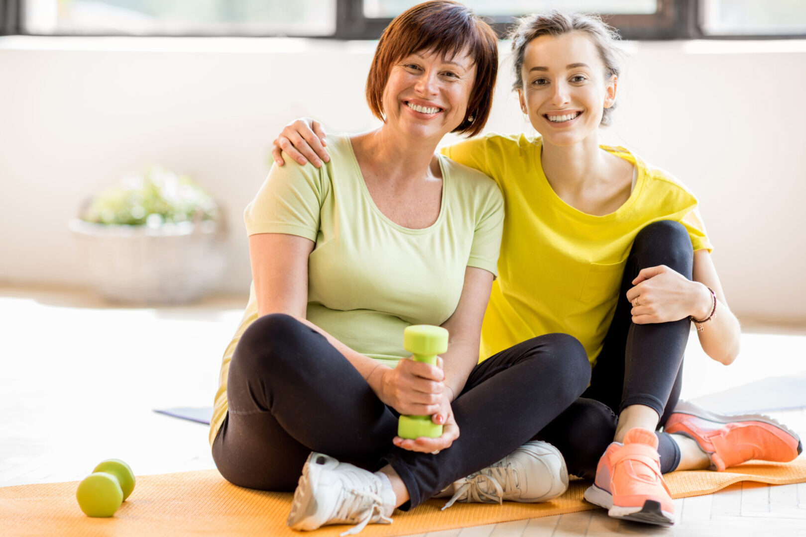 Two women sitting on the ground holding green cups.