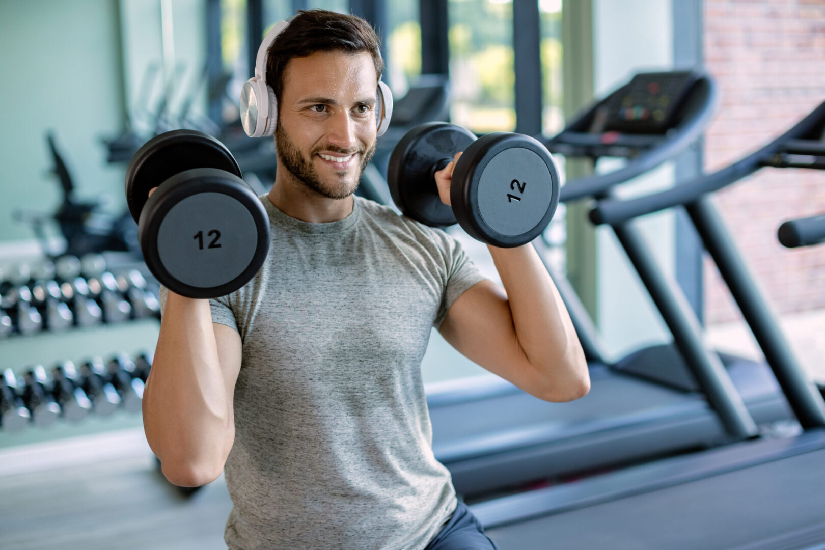 A man is holding two dumbbells while wearing headphones.